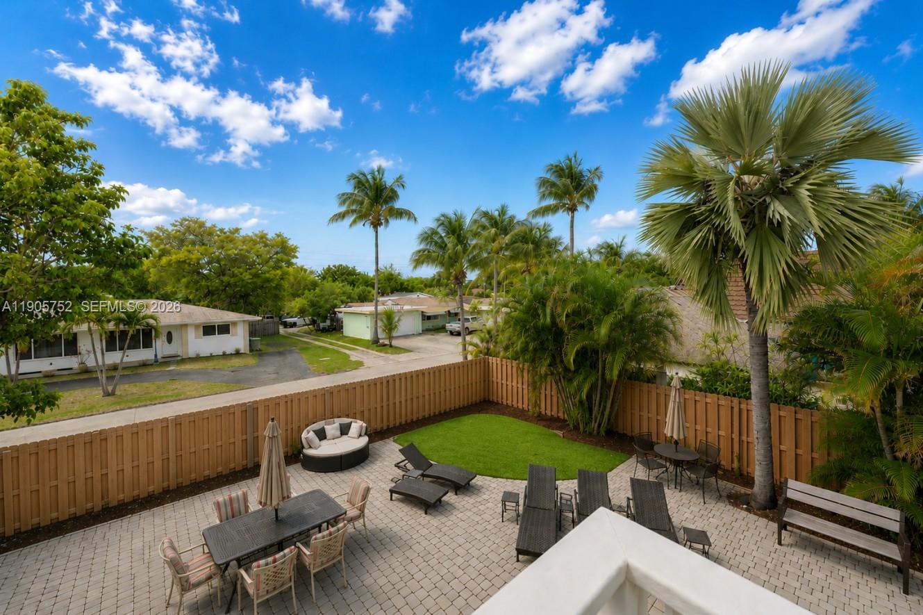 A backyard patio with outdoor furniture, a small lawn, and palm trees enclosed by fencing — 1690 NE 25th Ave, Pompano Beach FL 33062, POMPANO BEACH, FL