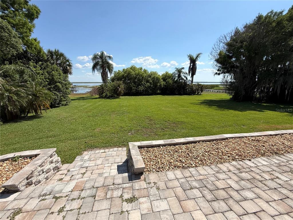 A paved patio overlooks a large grassy backyard leading to a lake — 1890 SAHA COURT, KISSIMMEE, FL