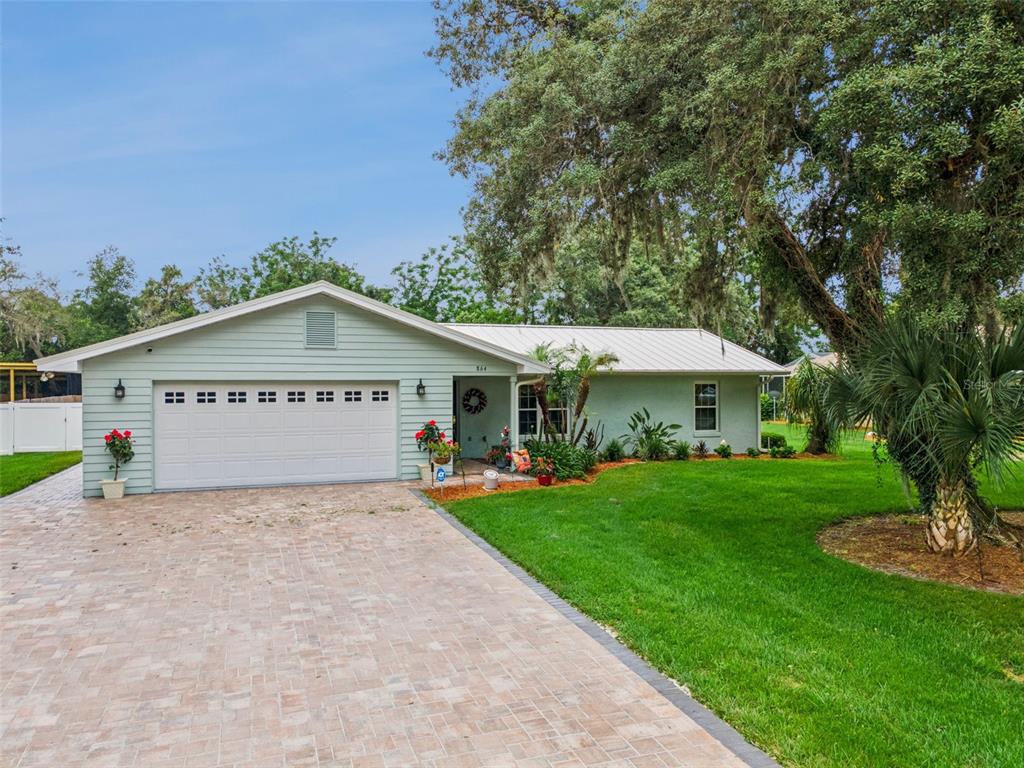 A light green single-story house features a white garage door and a brick paver driveway — 864 REDWOOD WAY, LAKE WALES, FL