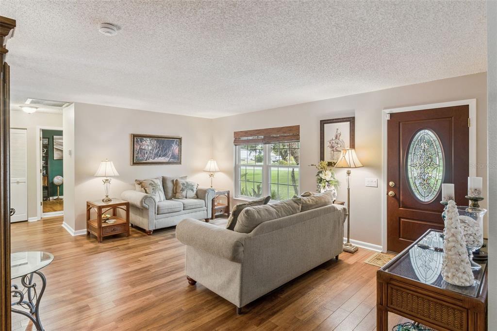 A living room with wood-look flooring, a sofa, a loveseat, and a front entry door — 864 REDWOOD WAY, LAKE WALES, FL