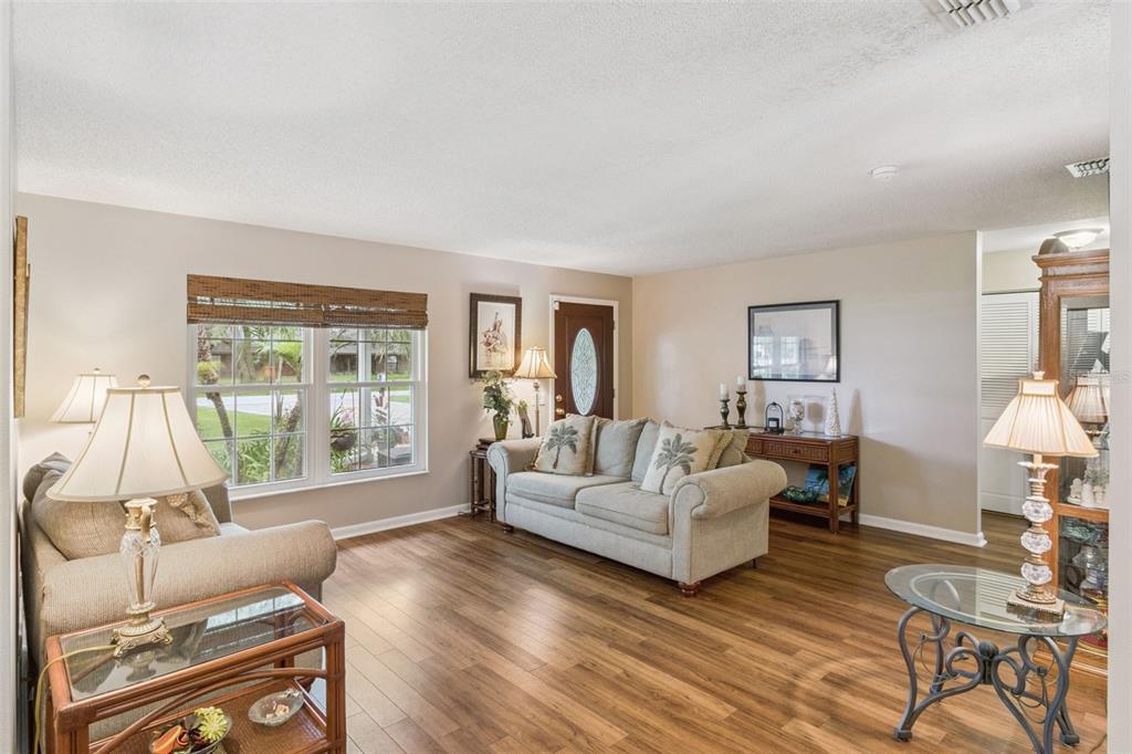 A living room with wood-look flooring, a beige sofa, and a front door — 864 REDWOOD WAY, LAKE WALES, FL
