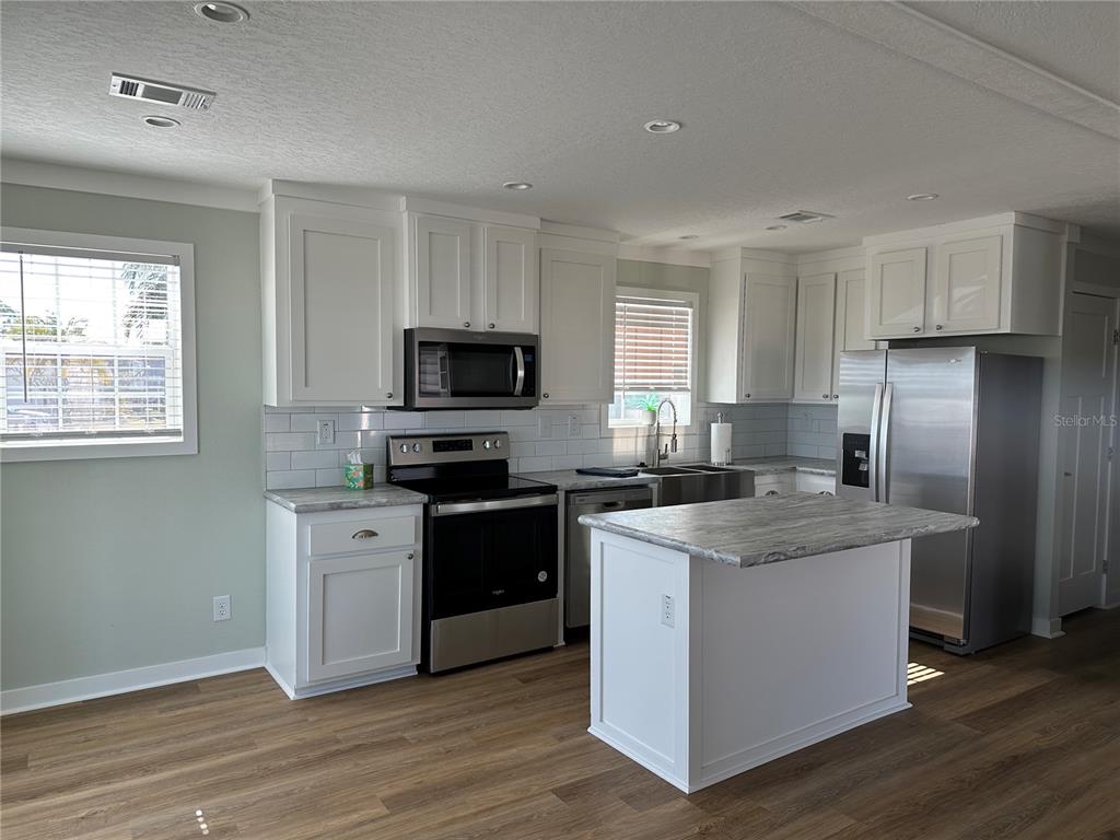 A kitchen with white cabinets, stainless steel appliances, a center island, and wood-look flooring — 330 TRAILORAMA DRIVE, NORTH PORT, FL