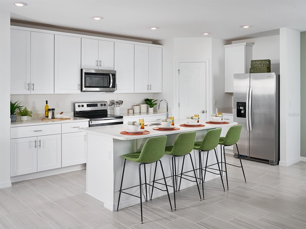 A modern kitchen features white cabinetry, stainless steel appliances, a center island, and green barstools — 2210 SAGELAND WAY, BARTOW, FL