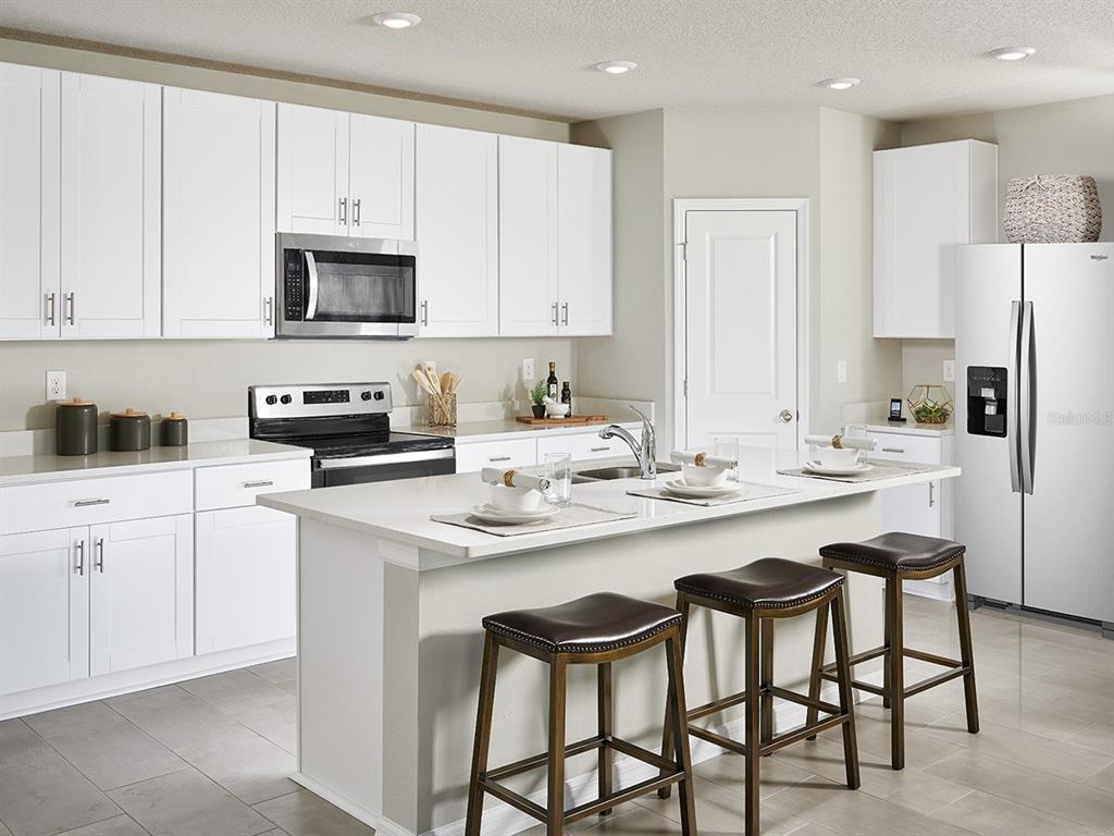 A modern kitchen features white cabinets, a central island with bar stools, and stainless appliances — 2210 SAGELAND WAY, BARTOW, FL