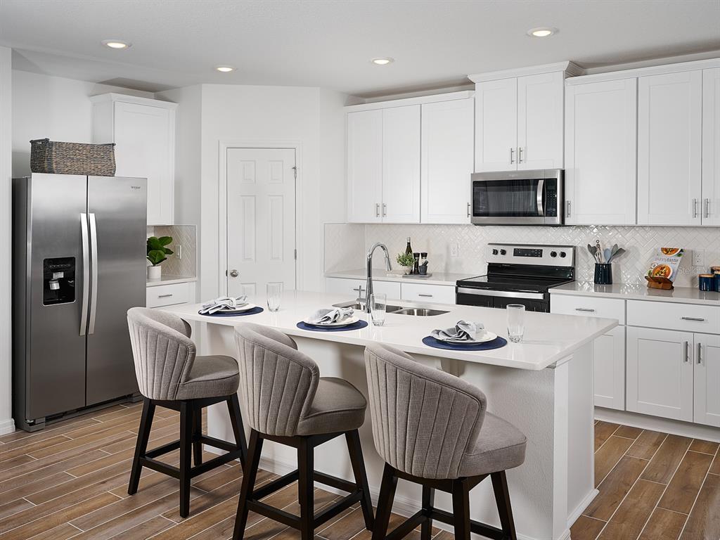 A modern kitchen features white cabinetry, stainless steel appliances, a central island, and bar seating — 2210 SAGELAND WAY, BARTOW, FL
