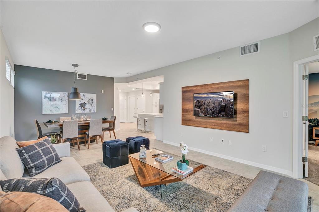 An open-concept living and dining area features a wood-paneled TV wall and neutral furniture — 4721 CLOCK TOWER DRIVE UNIT 108, KISSIMMEE, FL