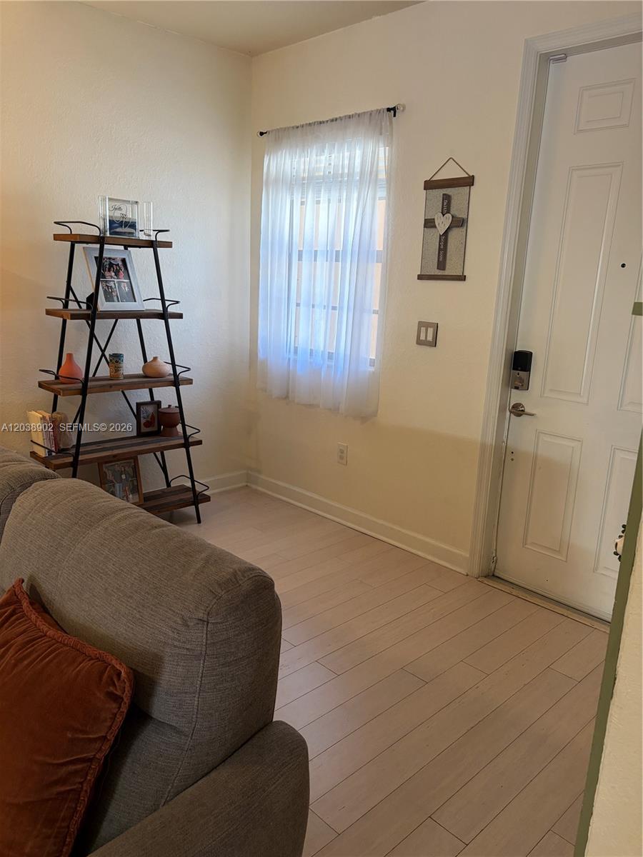 A living room features light wood-look flooring, a tall metal shelving unit, and a window — 370 NE 37th Pl, Homestead FL 33033, HOMESTEAD, FL