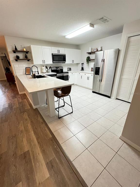 A kitchen features white cabinetry, a quartz-topped island with seating, and stainless steel appliances — 8837 GRAND PALMS CIRCLE UNIT A, KISSIMMEE, FL