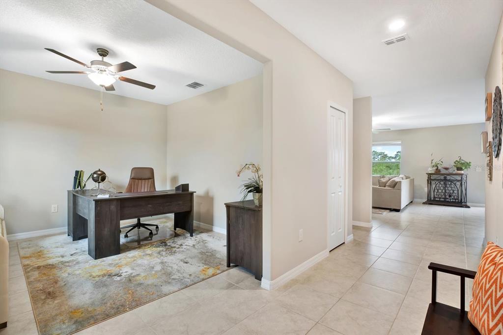A home office with a desk and area rug sits adjacent to a tiled hallway — 12813 WILDFLOWER MEADOW DRIVE, RIVERVIEW, FL