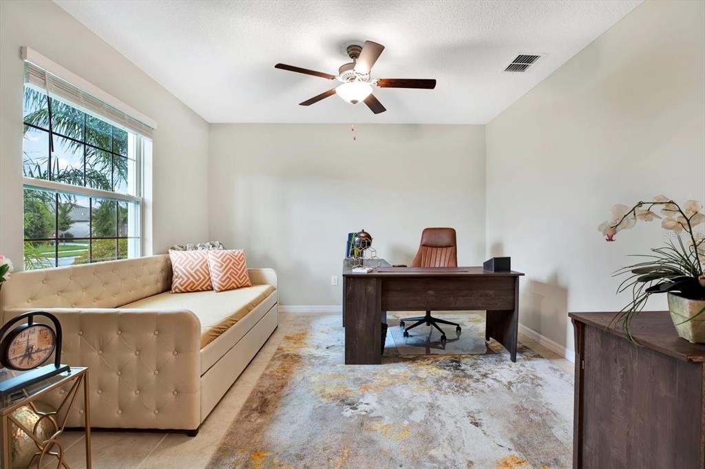 A home office features a daybed, a wooden desk with a chair, and a patterned rug — 12813 WILDFLOWER MEADOW DRIVE, RIVERVIEW, FL