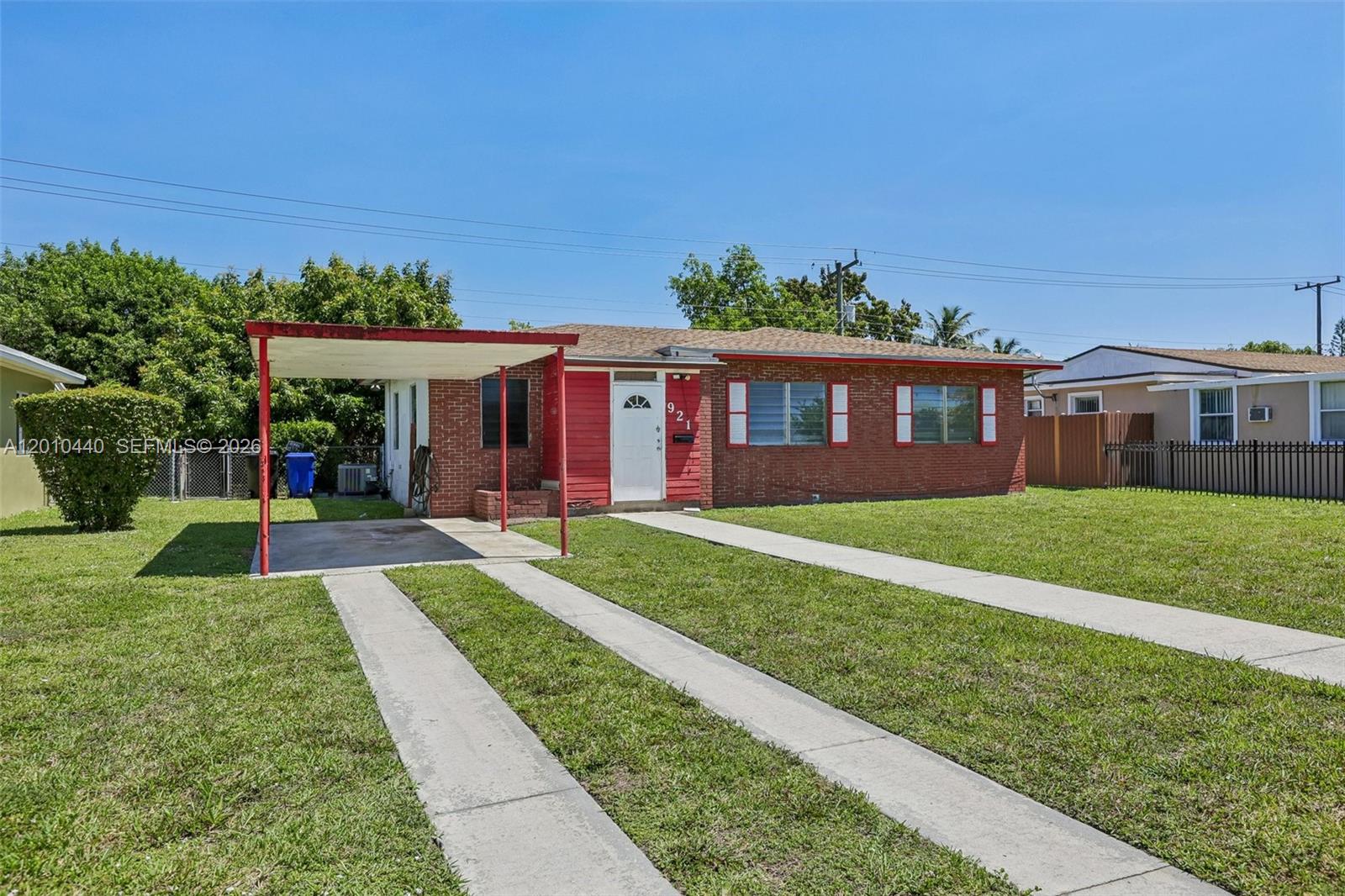 A single-story brick house features a red-trimmed carport, a concrete driveway, and white shutters — 921 NE 159th St, North Miami Beach FL 33162, NORTH MIAMI BEACH, FL