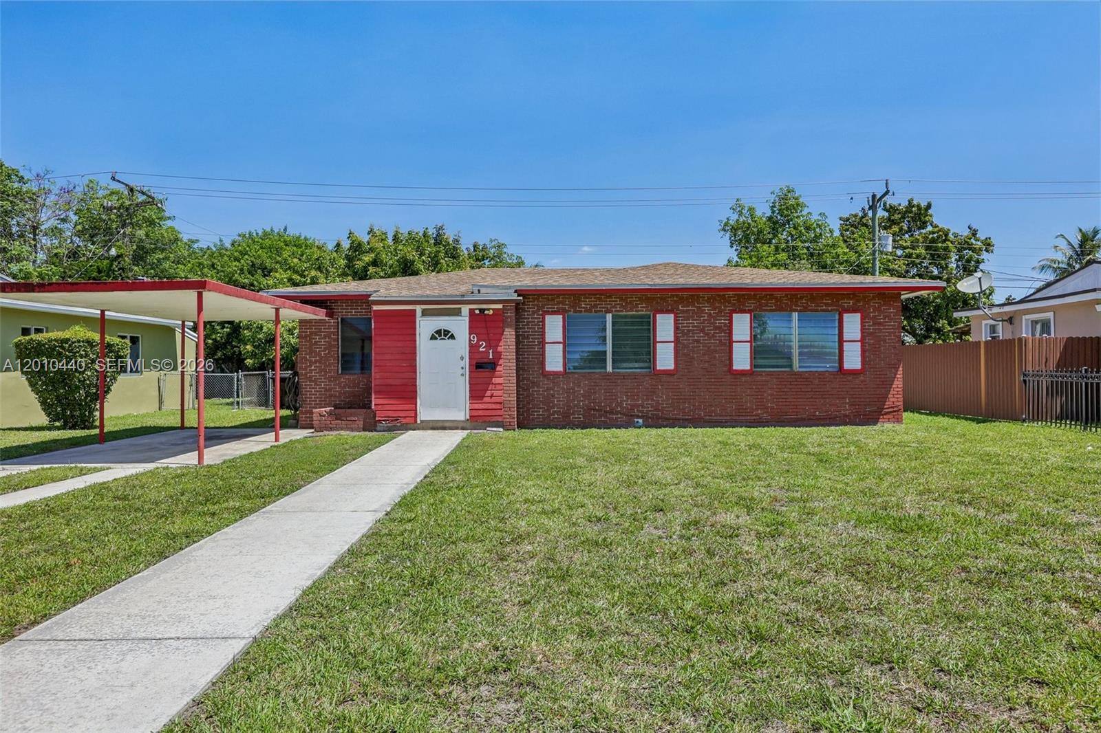 A single-story red brick house features a white front door and an attached metal carport — 921 NE 159th St, North Miami Beach FL 33162, NORTH MIAMI BEACH, FL