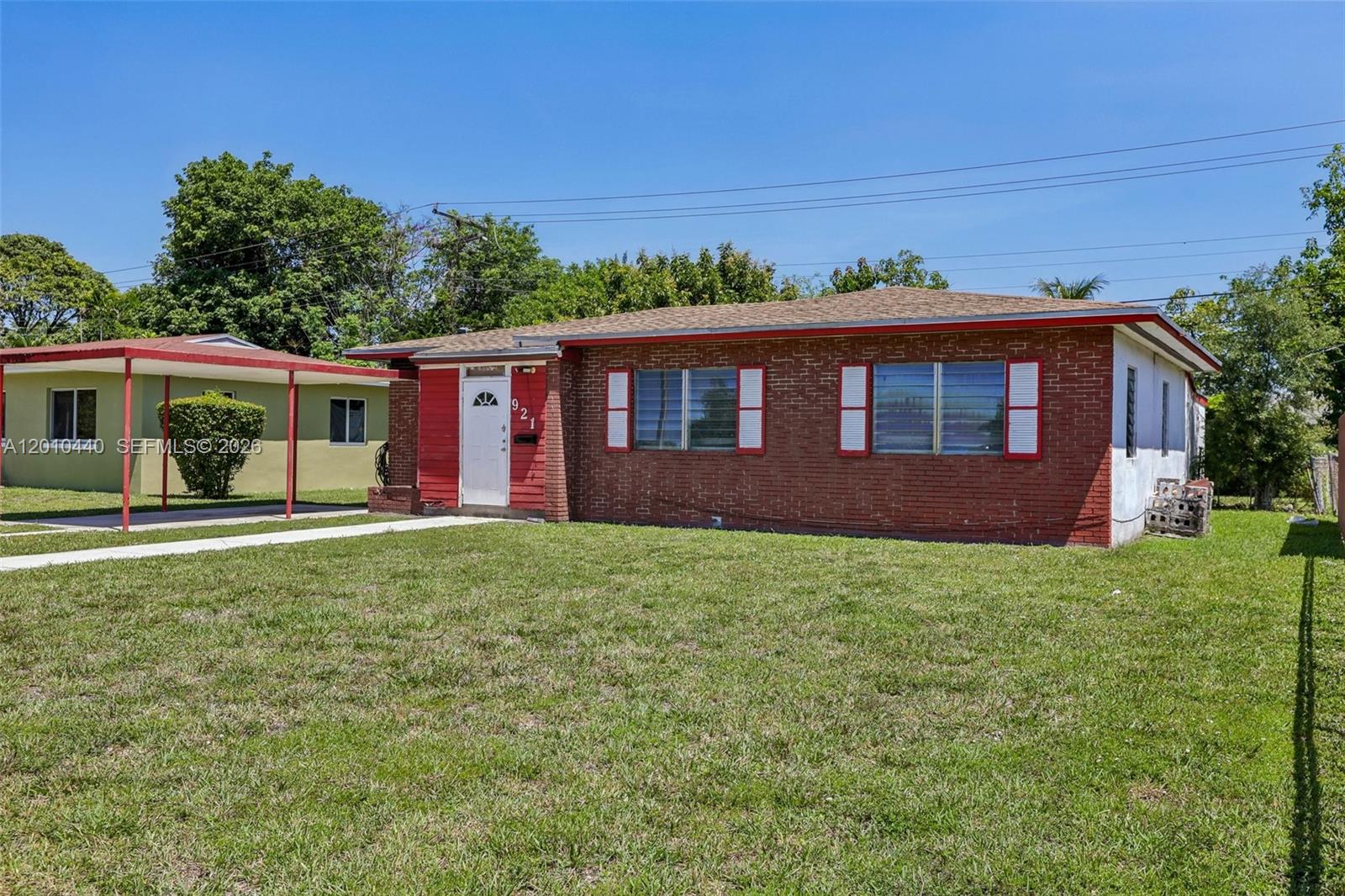 A single-story brick house features a red-trimmed entrance and an adjacent metal carport — 921 NE 159th St, North Miami Beach FL 33162, NORTH MIAMI BEACH, FL