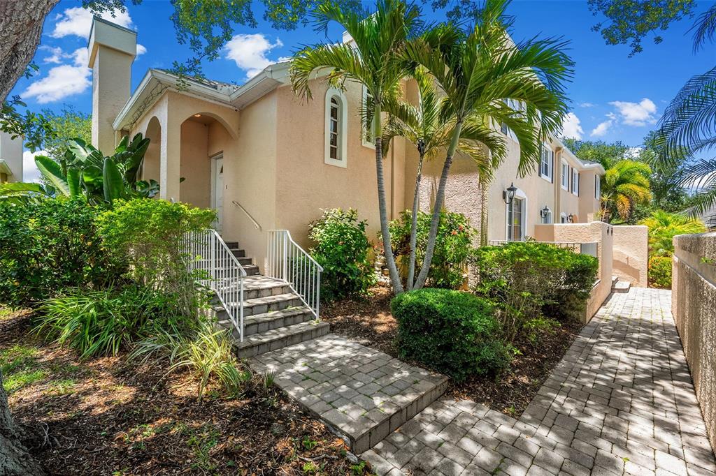 A tan two-story building with a paved walkway, stairs, and palm trees in the front — 13770 MARSEILLES COURT, CLEARWATER, FL