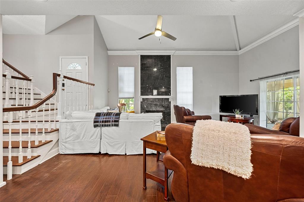 A living room features a vaulted ceiling, a dark stone fireplace, and a wooden staircase — 13770 MARSEILLES COURT, CLEARWATER, FL