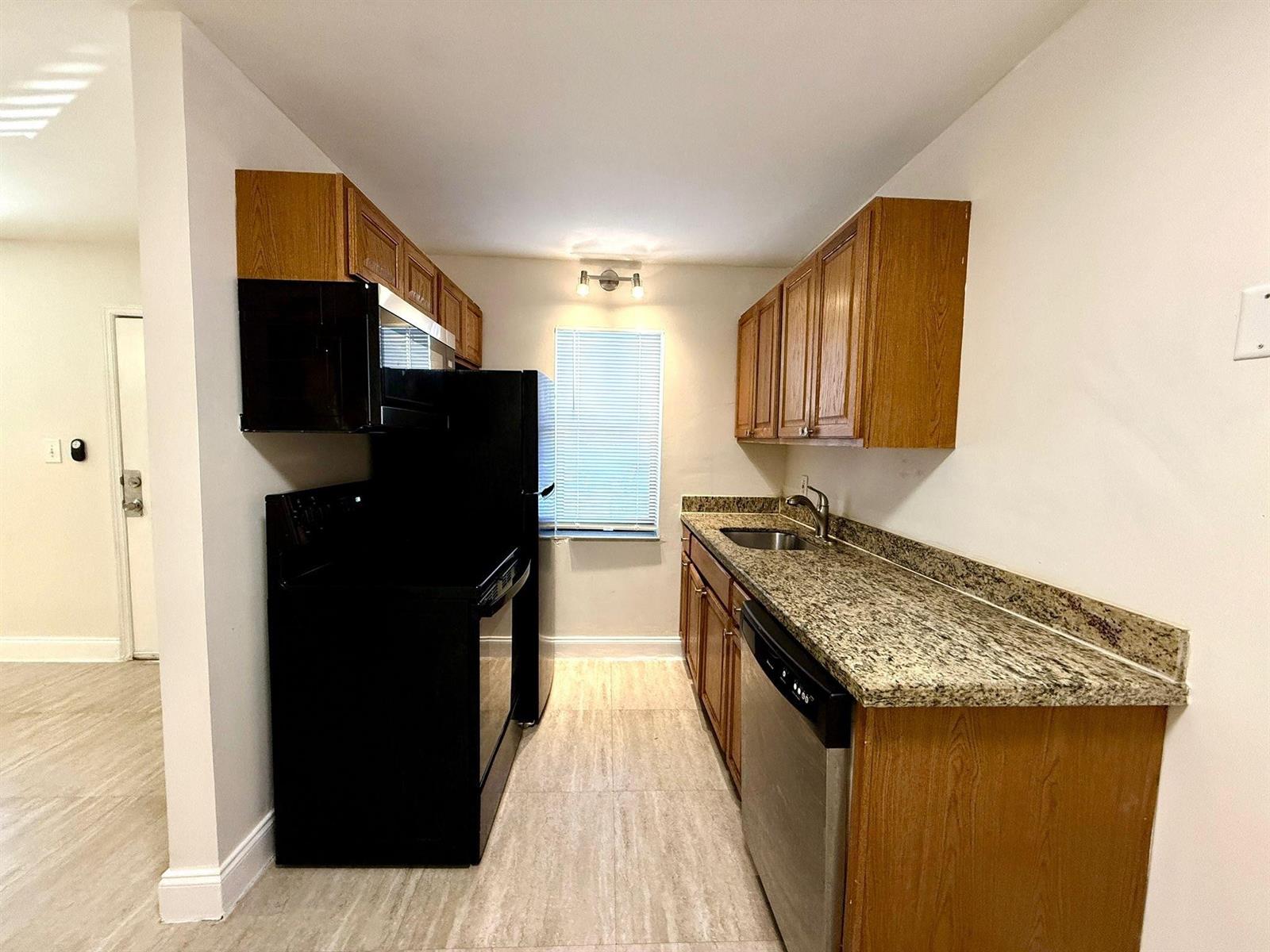 A galley kitchen features wood cabinets, granite countertops, and black appliances — 607 NE 29th Drive # 22, Wilton Manors FL 33334, WILTON MANORS, FL