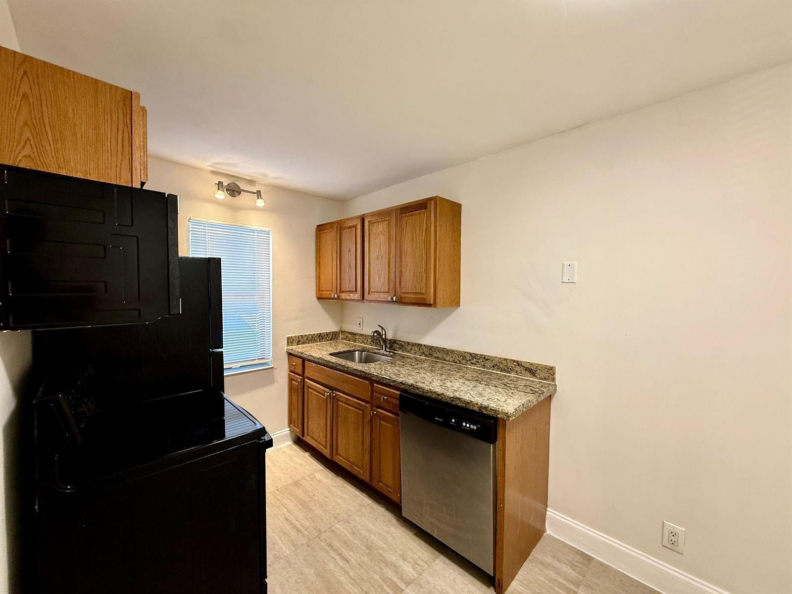 A kitchen features wood cabinets, granite countertops, a stainless steel dishwasher, and black appliances — 607 NE 29th Drive # 22, Wilton Manors FL 33334, WILTON MANORS, FL
