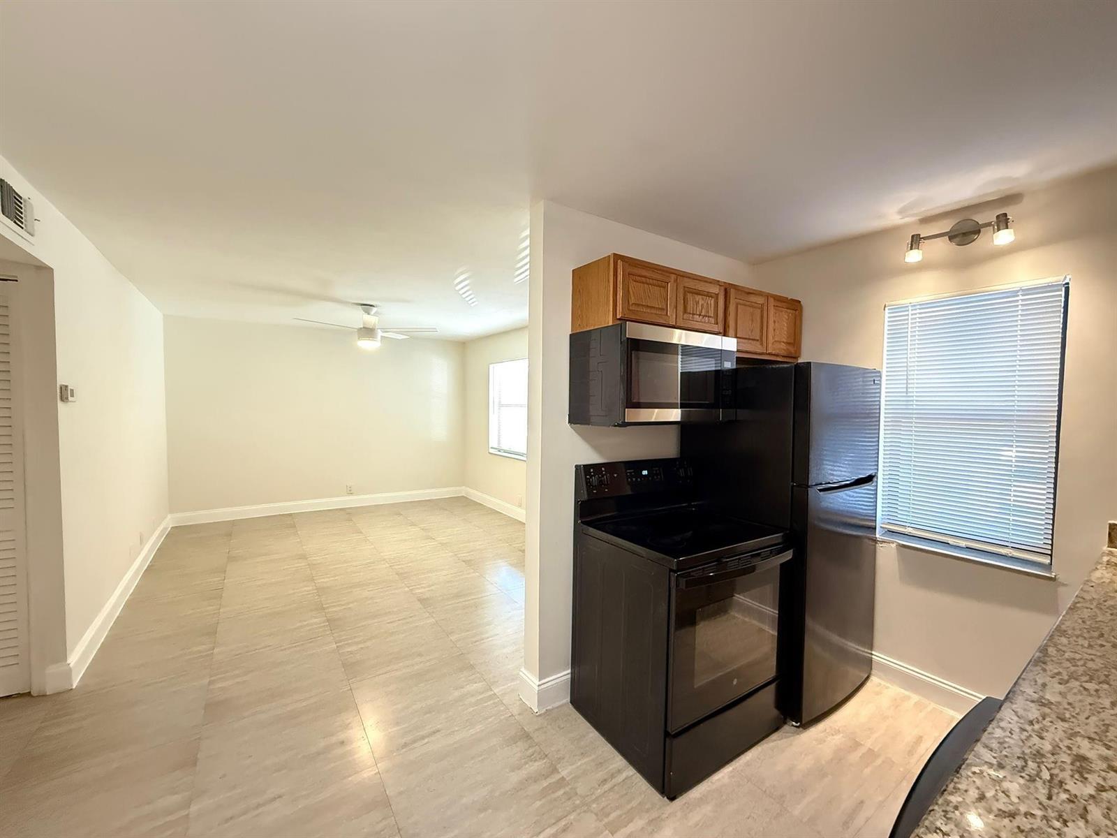 A kitchen with black appliances and wood cabinets opens into a living area with tile floors — 607 NE 29th Drive # 22, Wilton Manors FL 33334, WILTON MANORS, FL