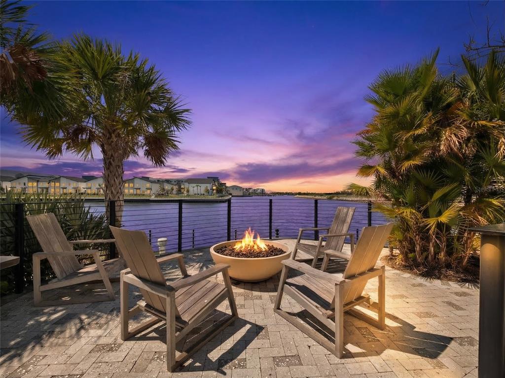 A patio with four wooden chairs surrounding a fire pit overlooking a lake at sunset — 5351 BRIDGE STREET UNIT 49, TAMPA, FL