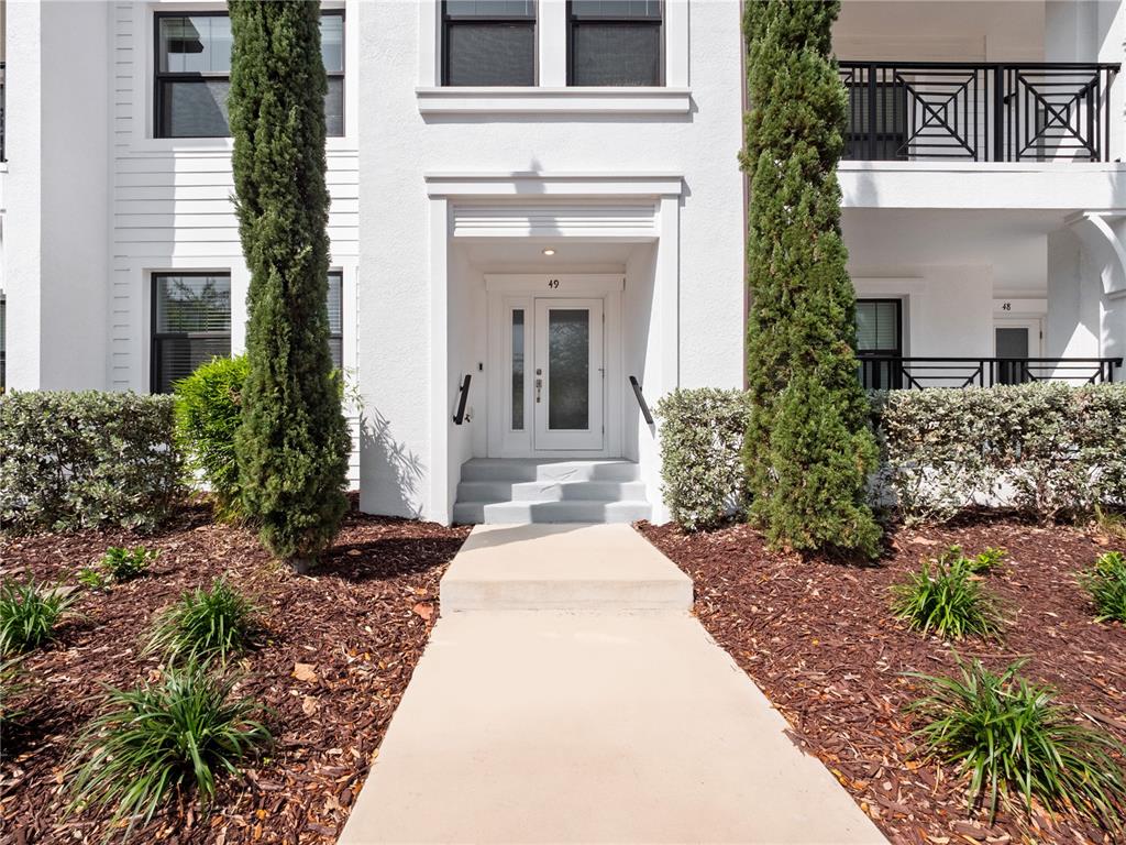 A white building exterior features a central entrance with steps and tall, thin evergreen trees — 5351 BRIDGE STREET UNIT 49, TAMPA, FL
