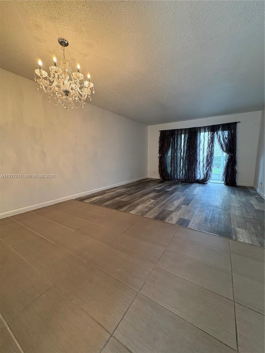 An open living area features a crystal chandelier, tile flooring, and wood-look laminate flooring — 4441 NW 16th St # J102, Lauderhill FL 33313, LAUDERHILL, FL