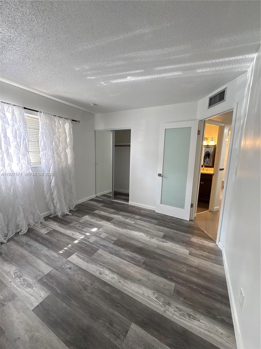 A bedroom features gray wood-look flooring, white walls, a mirrored closet, and a frosted glass door — 4441 NW 16th St # J102, Lauderhill FL 33313, LAUDERHILL, FL