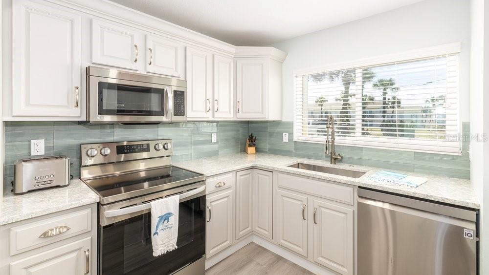 A kitchen features white cabinets, stainless steel appliances, granite countertops, and a blue tile backsplash — 4783 S ATLANTIC AVENUE UNIT E2, PORT ORANGE, FL