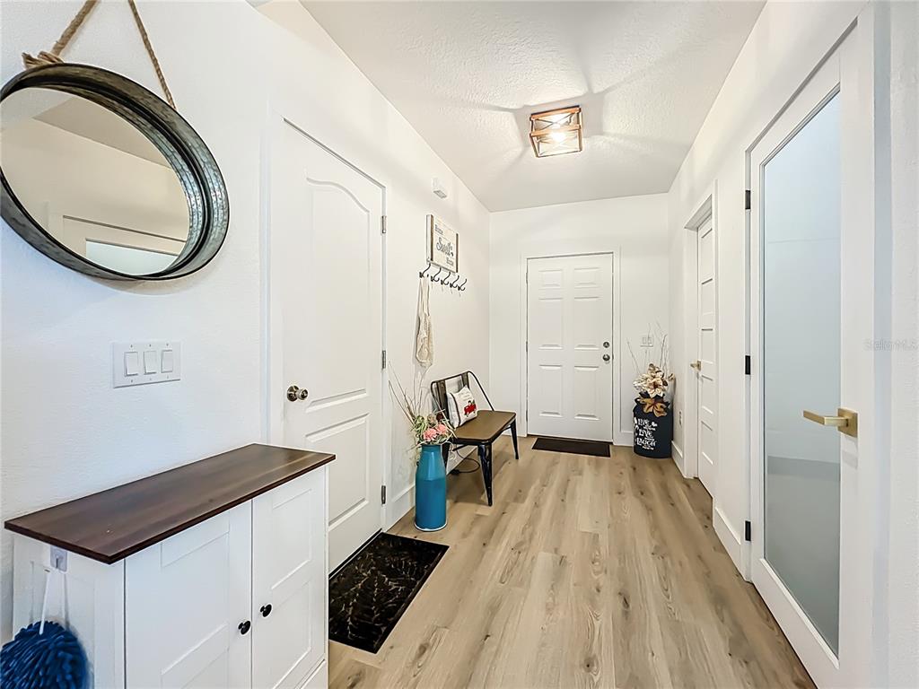 A bright entryway features light wood-look flooring, a white cabinet, a bench, and a mirror — 9219 CANNA STREET, PORT CHARLOTTE, FL