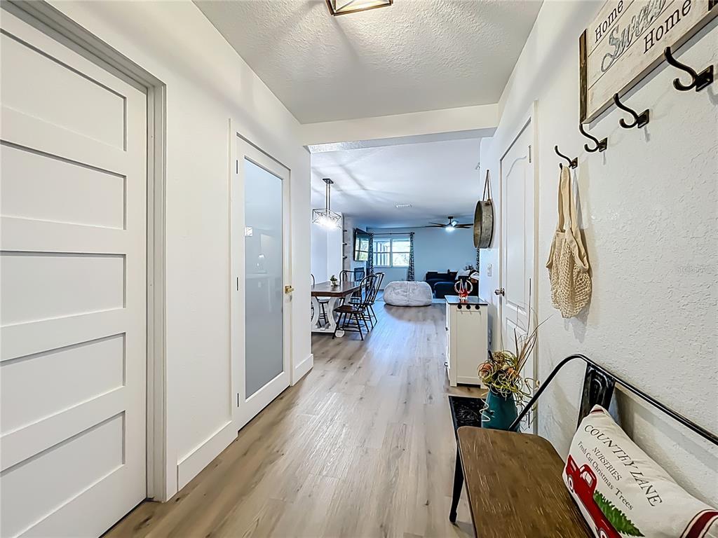 A bright hallway with light wood-look flooring leads into an open-concept dining and living area — 9219 CANNA STREET, PORT CHARLOTTE, FL