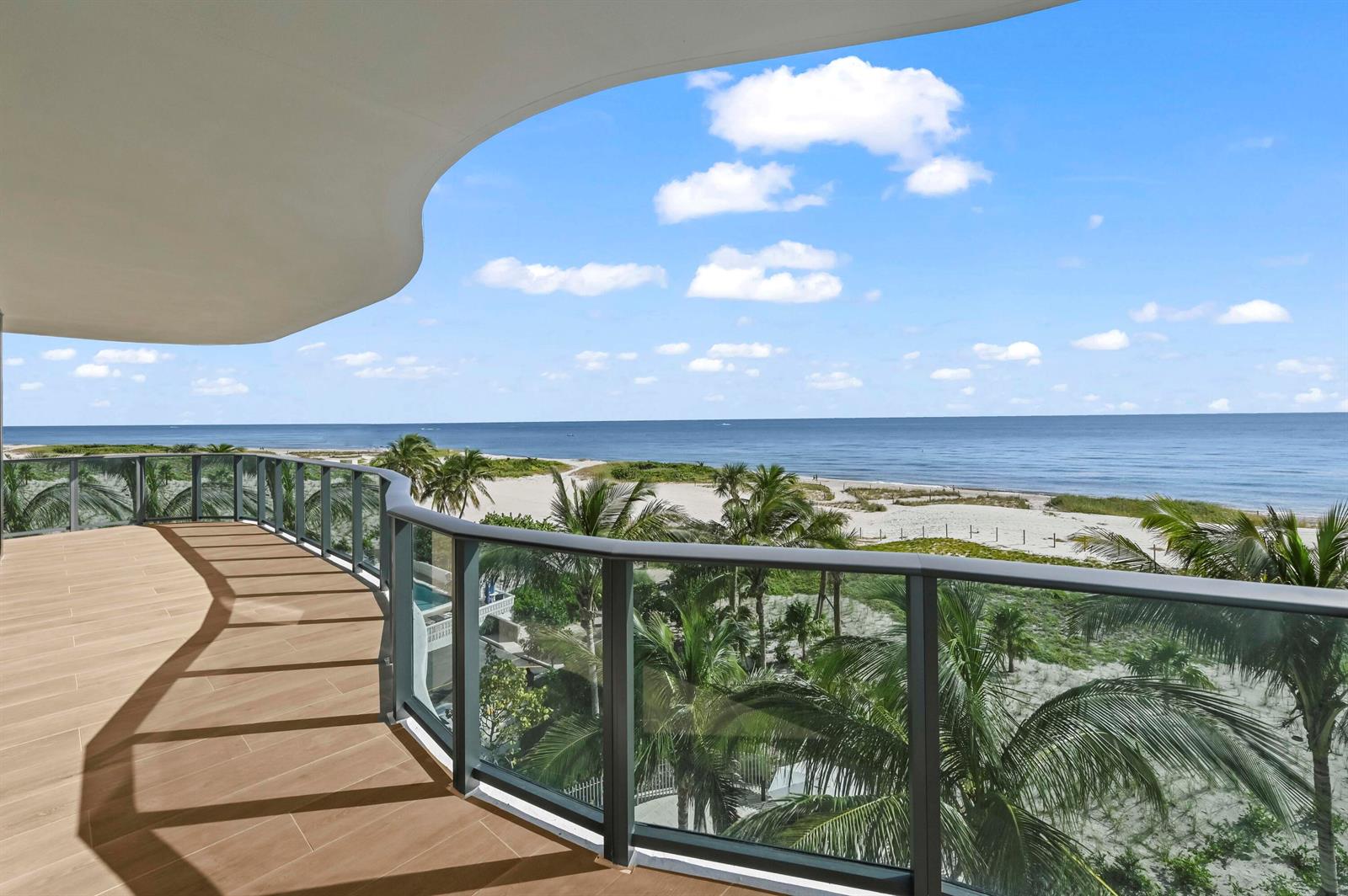 A curved balcony with wood-look tile flooring overlooks a sandy beach and the ocean — 900 N Ocean Boulevard # 406, Pompano Beach FL 33062, POMPANO BEACH, FL
