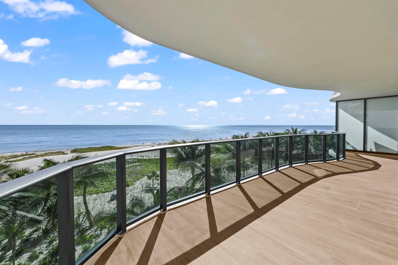 A spacious balcony with wood-look tile flooring and a glass railing overlooking the ocean — 900 N Ocean Boulevard # 406, Pompano Beach FL 33062, POMPANO BEACH, FL