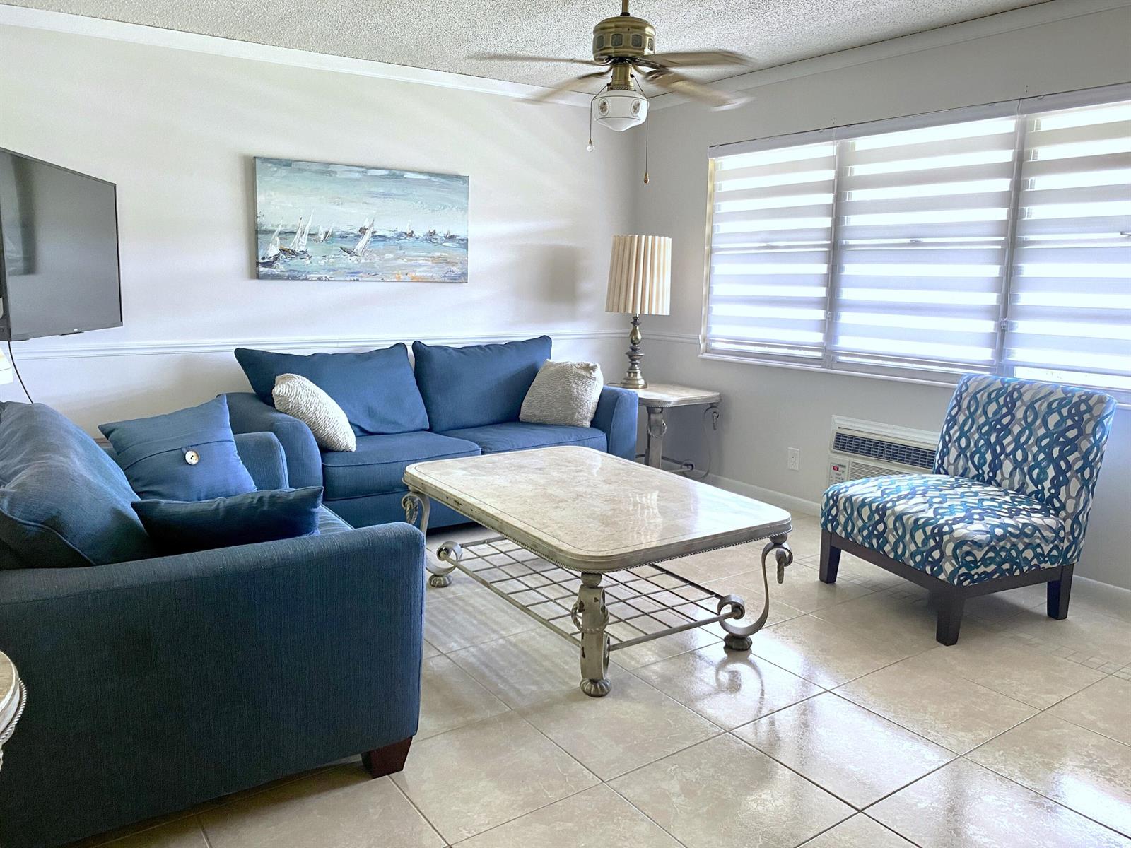A living room features blue sofas, a patterned armchair, a coffee table, and tile flooring — 335 Farnham P, Deerfield Beach FL 33442, DEERFIELD BEACH, FL