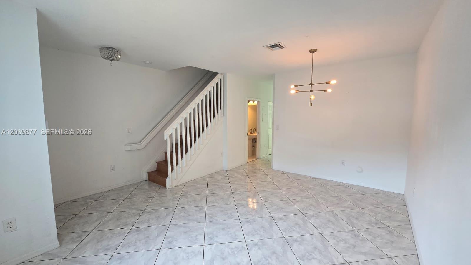 An interior view shows a tiled living area with a staircase and a modern chandelier — 5791 NW 116th Ave # 101, Doral FL 33178, DORAL, FL