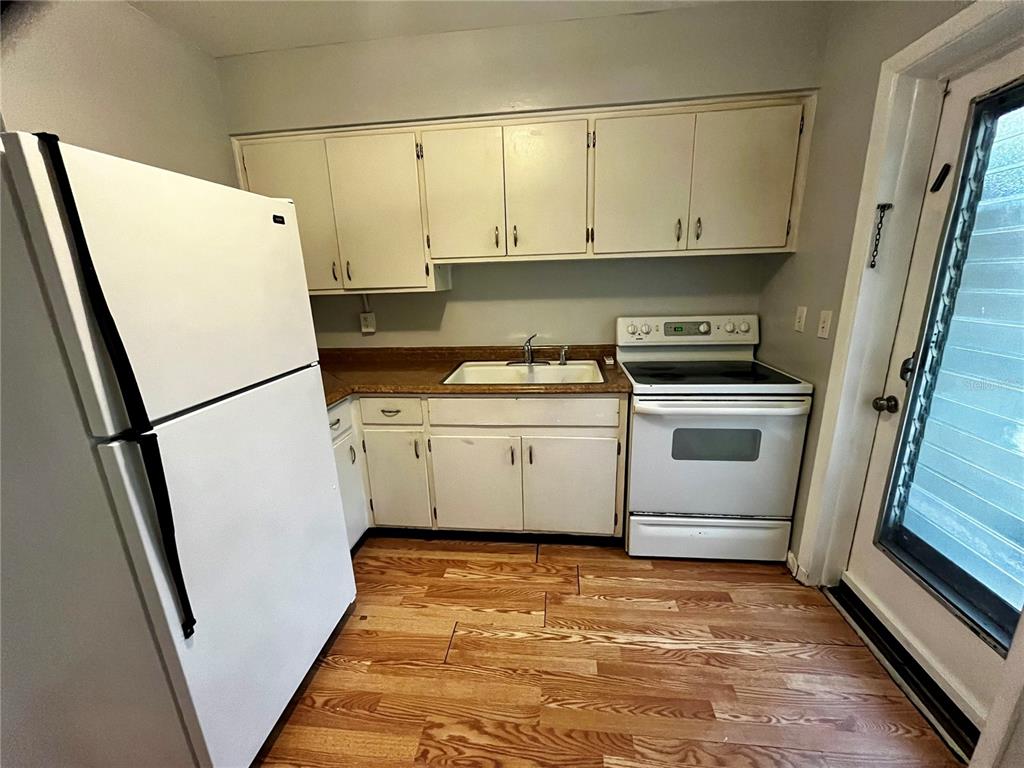 A kitchen features white appliances, light-colored cabinets, a sink, and wood-look flooring — 1411 KENNYWOOD DRIVE Apt B, LARGO, FL
