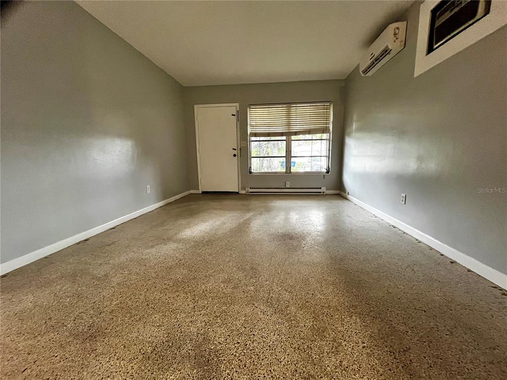 An empty room with grey walls, a concrete floor, a window, and a wall-mounted air conditioner — 1411 KENNYWOOD DRIVE Apt B, LARGO, FL