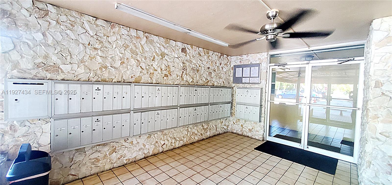 An indoor mailroom features stone walls, tiled flooring, a ceiling fan, and glass entry doors — 3905 N Nob Hill Rd # 510, Sunrise FL 33351, SUNRISE, FL