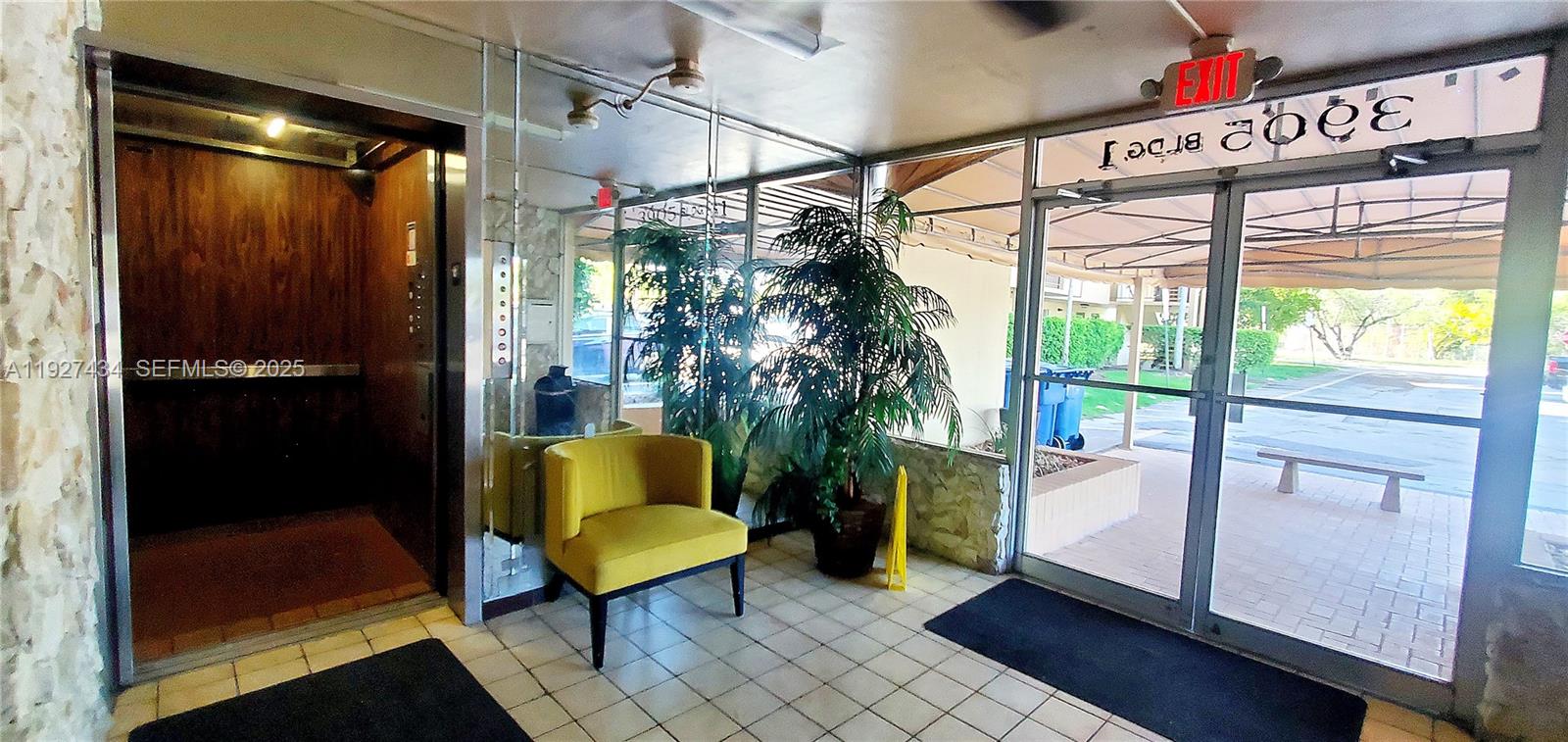 A building lobby features a yellow chair, a potted plant, an elevator, and glass doors — 3905 N Nob Hill Rd # 510, Sunrise FL 33351, SUNRISE, FL