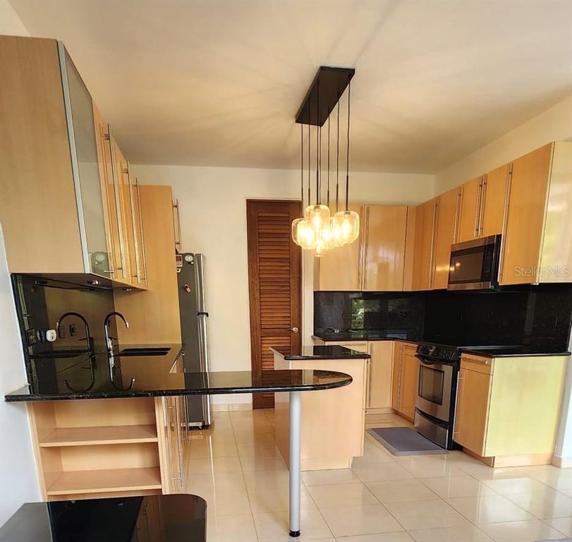 A kitchen features light wood cabinets, black countertops, a breakfast bar, and a pendant light — 1 AVENIDA PALMA REAL UNIT 404, GUAYNABO, PR