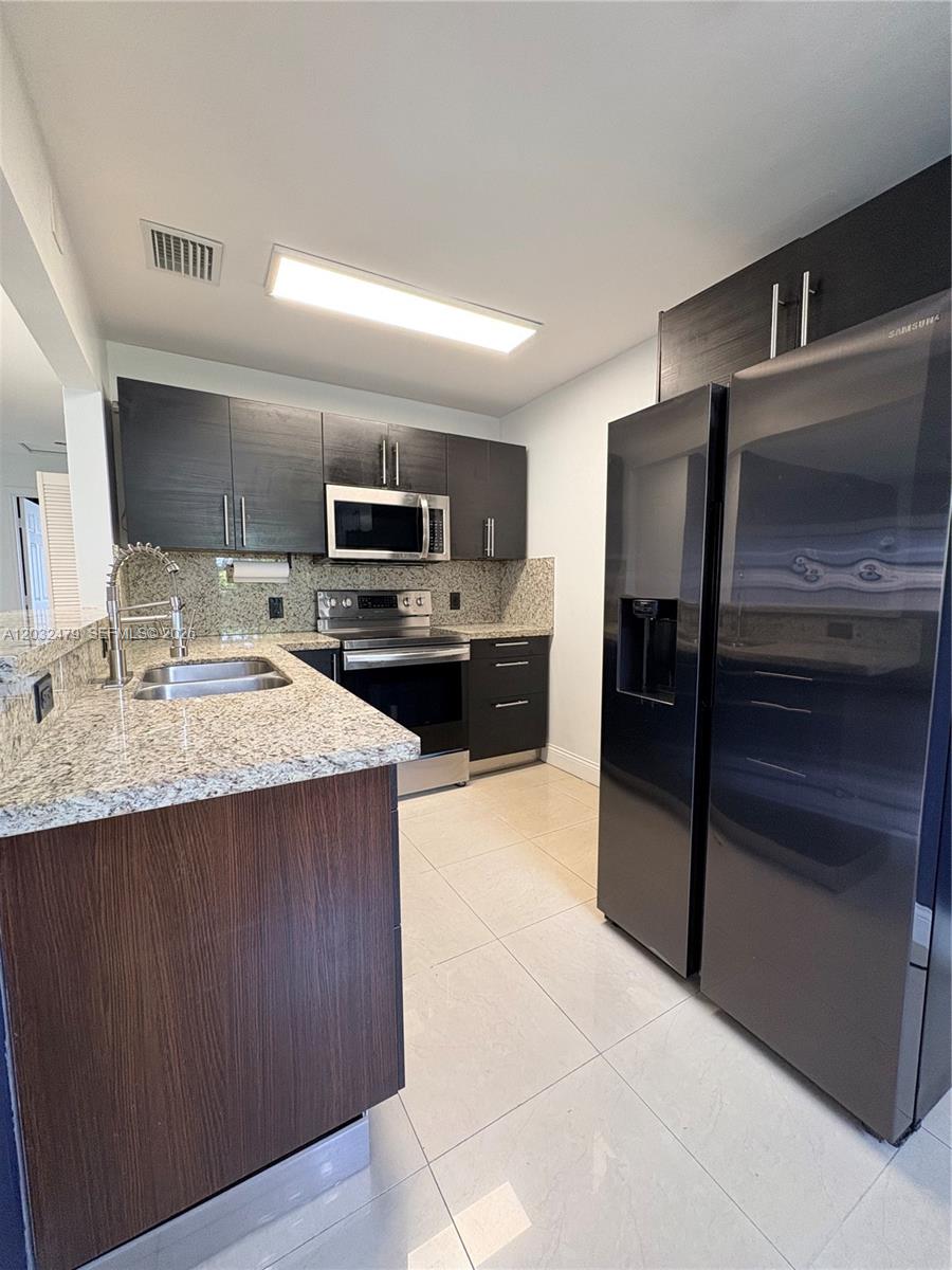 A kitchen features dark wood cabinets, granite countertops, stainless steel appliances, and light tile flooring — 1116 N 61st Ave # 1, Hollywood FL 33024, HOLLYWOOD, FL