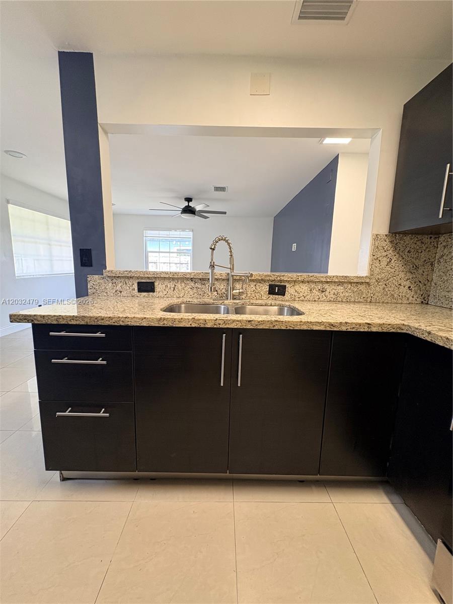 A kitchen features dark cabinets, granite countertops, and a pass-through window to the living area — 1116 N 61st Ave # 1, Hollywood FL 33024, HOLLYWOOD, FL
