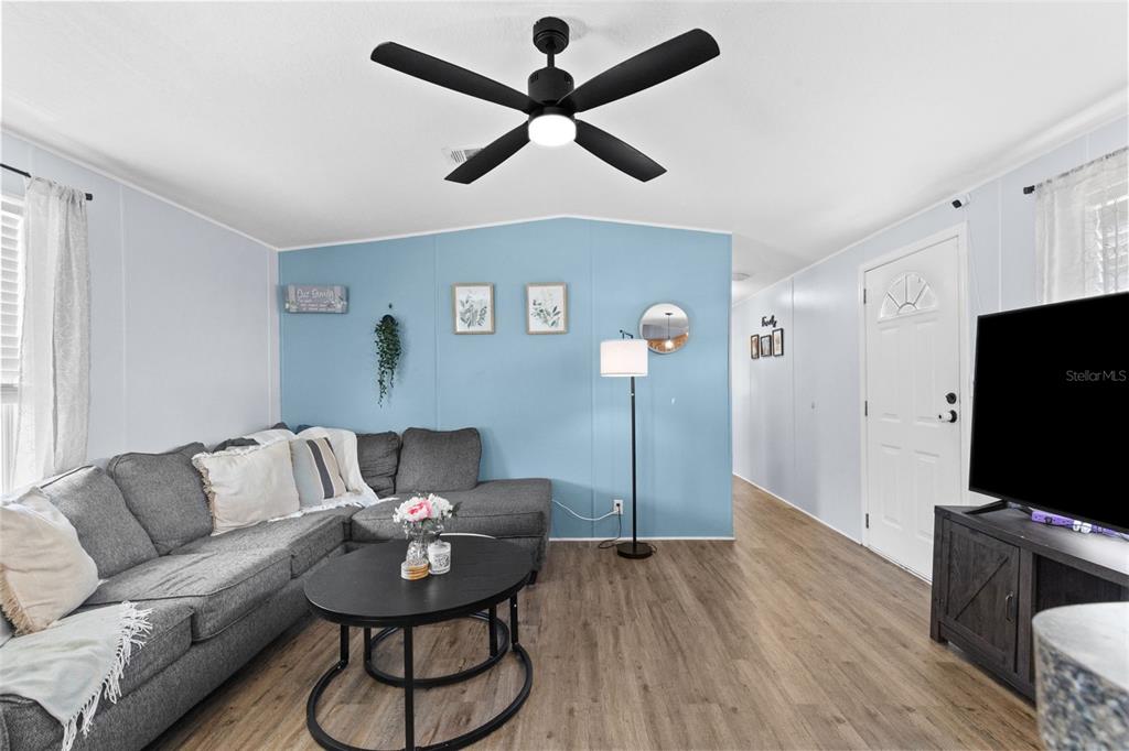 A living room features a grey sectional sofa, a blue accent wall, and wood-look flooring — 11535 LEANNE LANE UNIT 160, TAMPA, FL