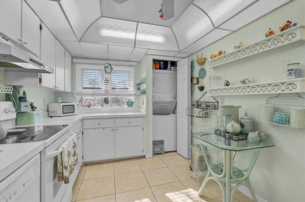 A kitchen with white cabinets, tile flooring, a glass table, and a stacked laundry unit — 93 BOUNDARY BOULEVARD UNIT 303, ROTONDA WEST, FL