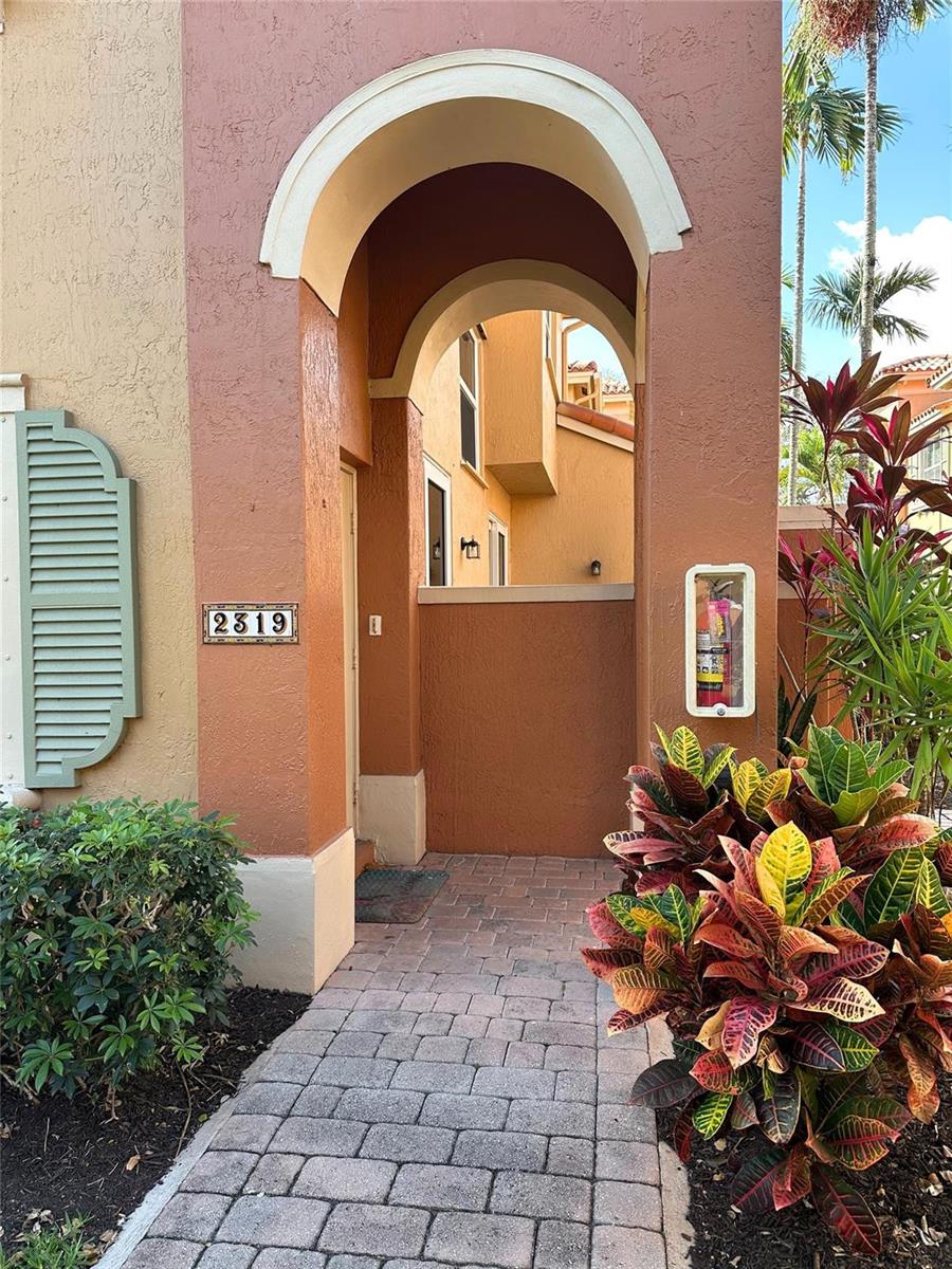 A paved walkway leads to an arched entryway with a fire extinguisher mounted on the wall — 2319 Clipper Place # 4510, Dania Beach FL 33312, DANIA BEACH, FL