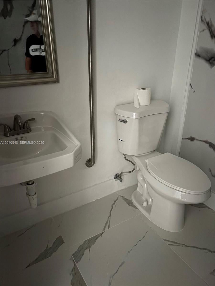 A bathroom features a wall-mounted sink, a toilet, and white marble-patterned floor tiles — 285 NW 27th Ave, Miami FL 33125, MIAMI, FL
