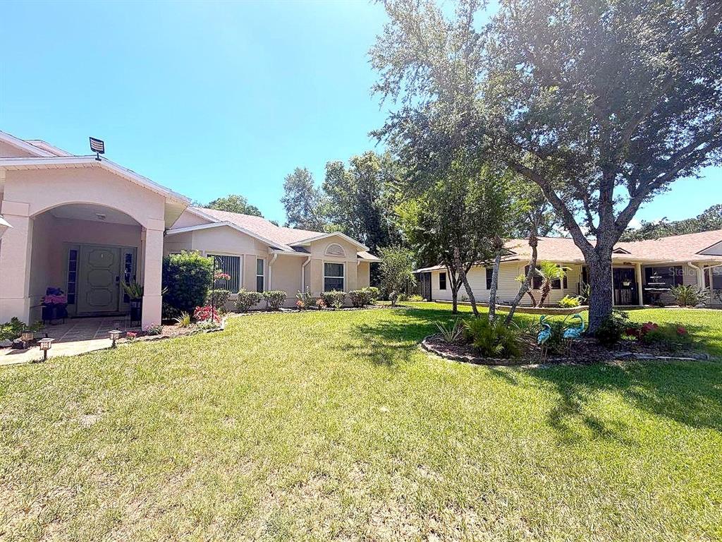A view of a single-story house exterior with a lawn, trees, and a covered entryway — 26912 BECKER COURT, LEESBURG, FL