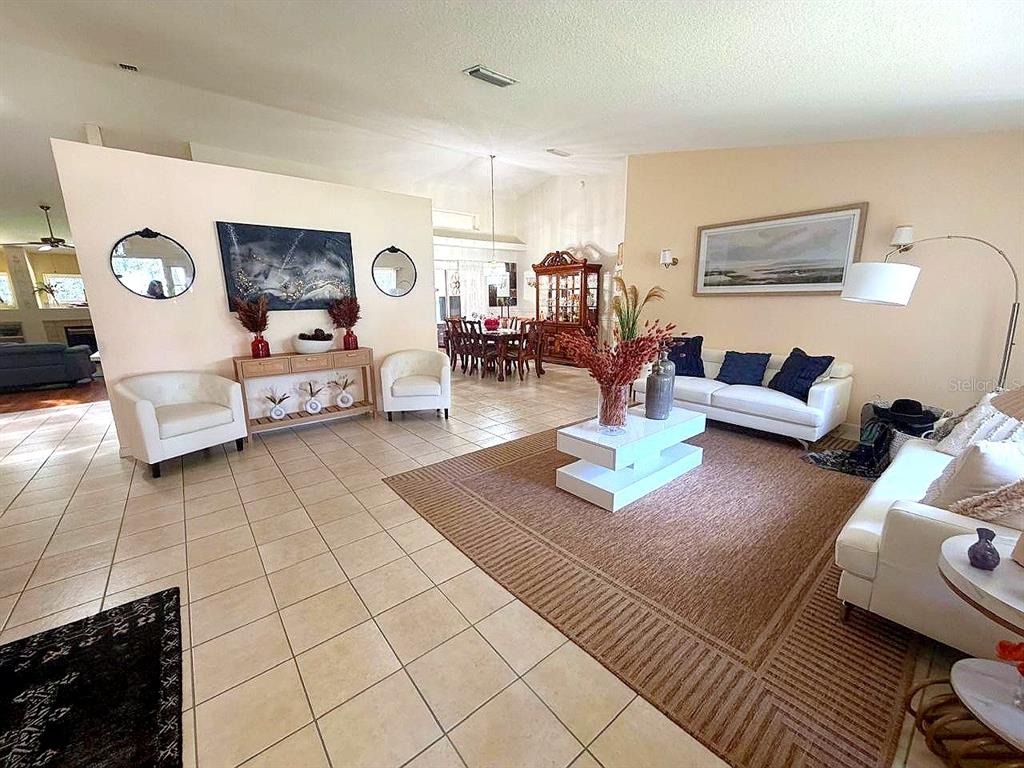 A living room with tile flooring, white sofas, a coffee table, and a dining area — 26912 BECKER COURT, LEESBURG, FL