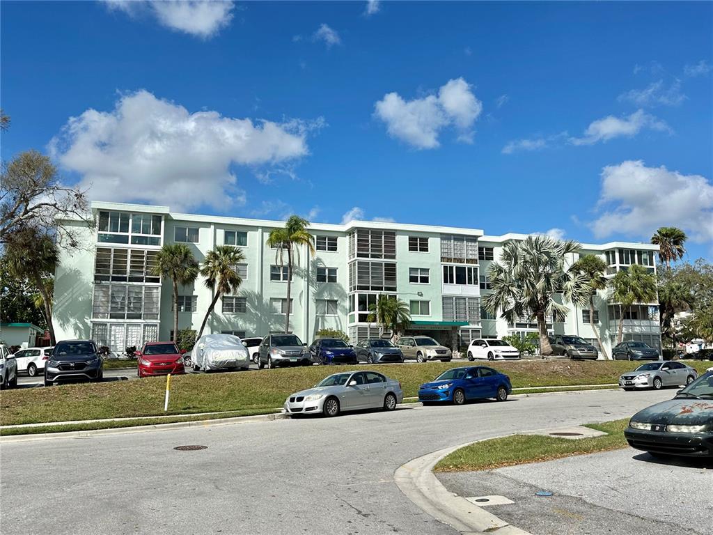 A multi-story apartment building with a light green facade and surrounding parking lot — 100 WAVERLY WAY UNIT 302, CLEARWATER, FL