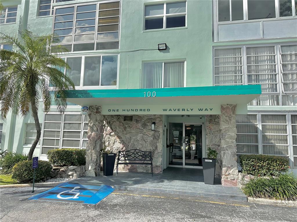 The exterior of a multi-story apartment building features a stone-accented entrance with a green awning — 100 WAVERLY WAY UNIT 302, CLEARWATER, FL