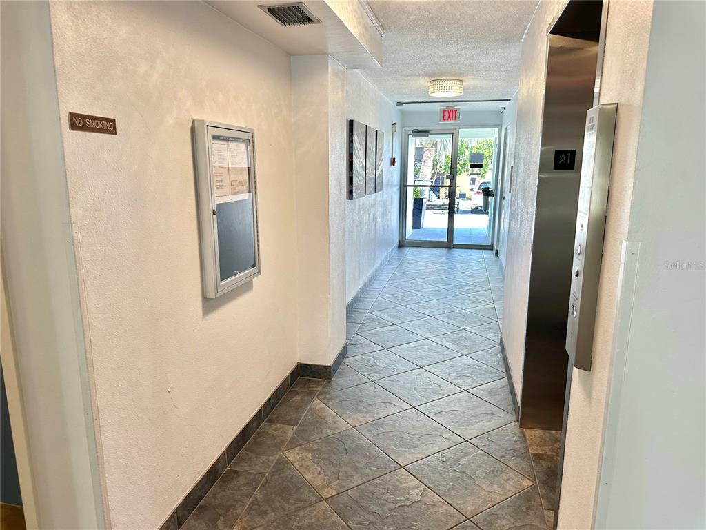 A hallway with tiled floors leads to a glass exit door near an elevator — 100 WAVERLY WAY UNIT 302, CLEARWATER, FL