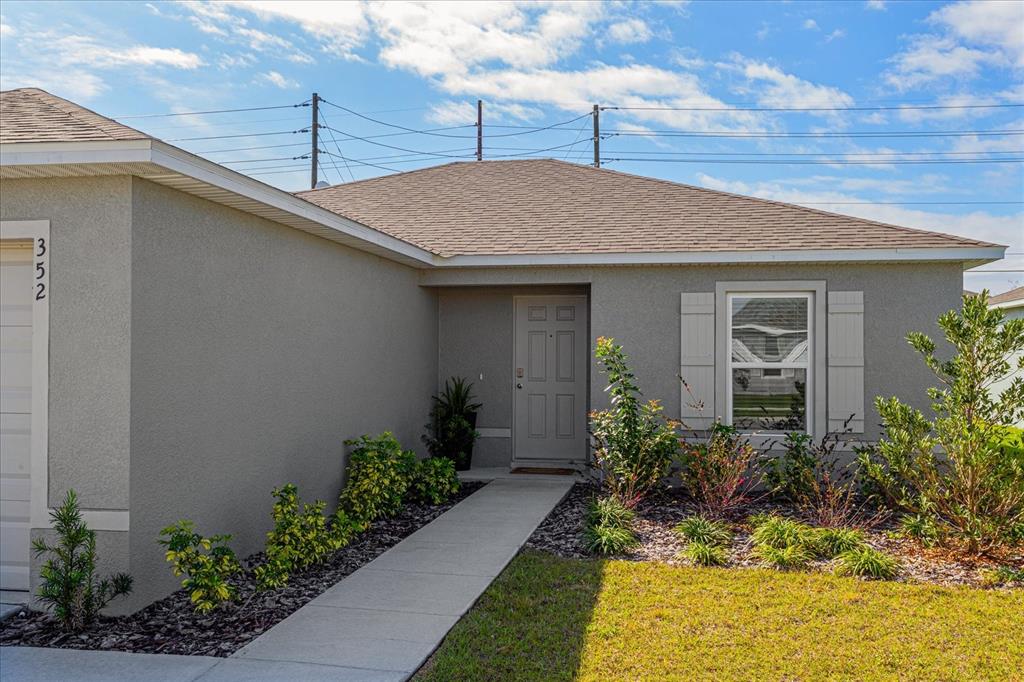A gray stucco house features a front walkway, a single door, and a small garden — 352 TOWNS CIRCLE, HAINES CITY, FL